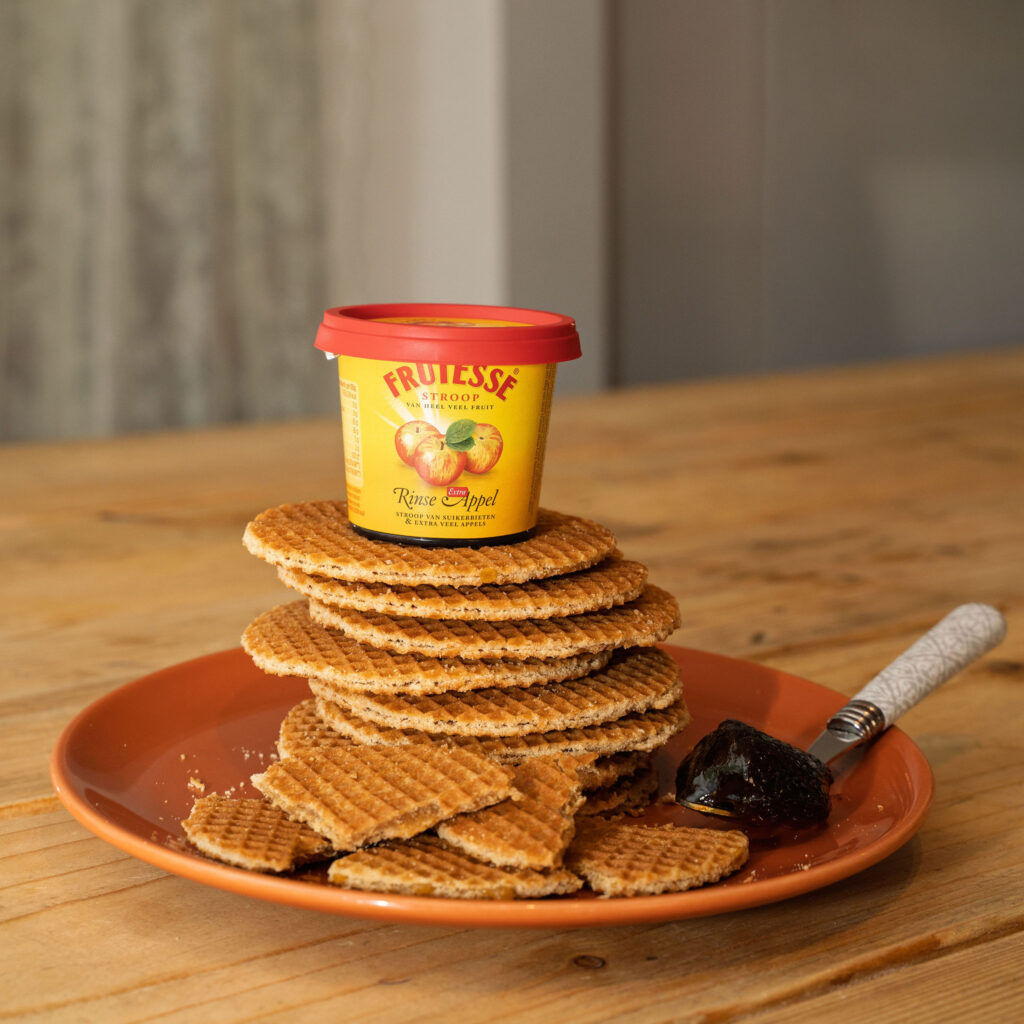 Stapel hollandse stroopwafels op een terracotta bord met een potje Frutesse Rinse Appelstroop bovenop.