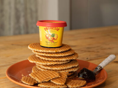 Stapel hollandse stroopwafels op een terracotta bord met een potje Frutesse Rinse Appelstroop bovenop.